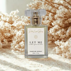 Clear glass perfume bottle with gold fine mist sprayer labeled “Let Me Make You Smile,” a soft floral, aquatic, amber fragrance inspired by romance and music.
